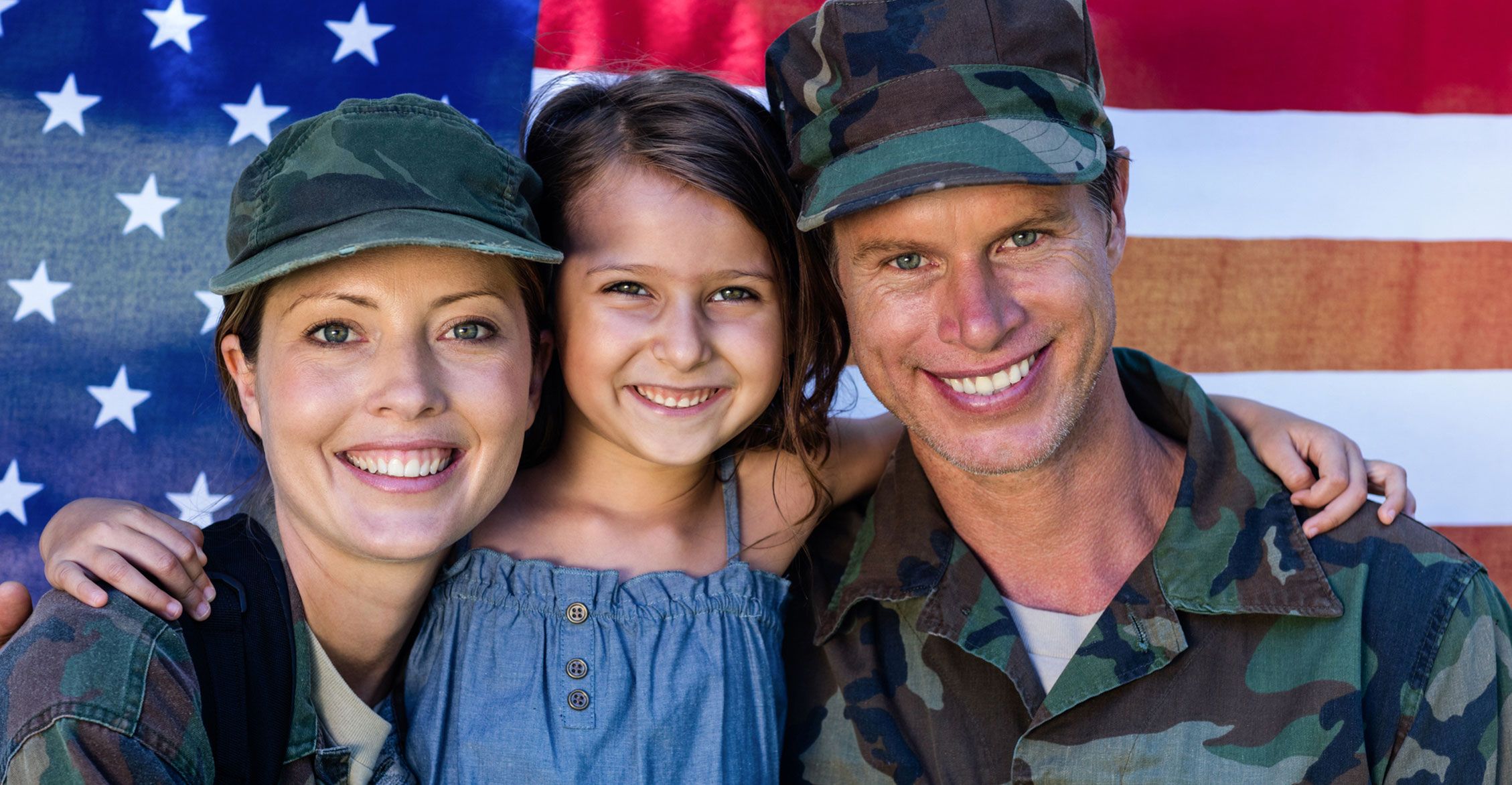 Man and woman in military fatigues against an American flag with a young girl in between them 